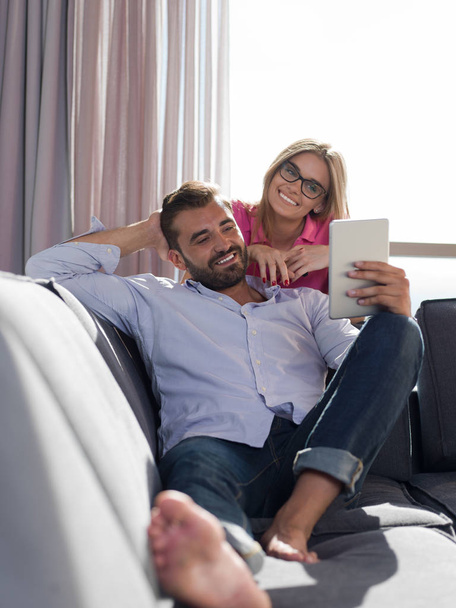 Young couple relaxing at  home using tablet computers reading in the living room on the sofa couch. - Fotoğraf, Görsel