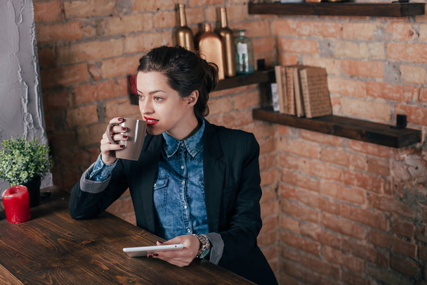 Beautiful young female freelancer with notepad and tablet have a coffee break in loft interior room - Foto, imagen