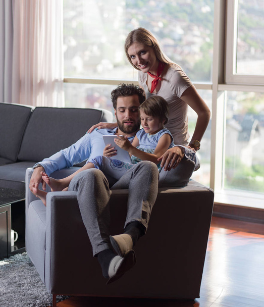 Glückliche junge Familie spielt mit Tablet zu Hause auf dem Sofa - Foto, Bild