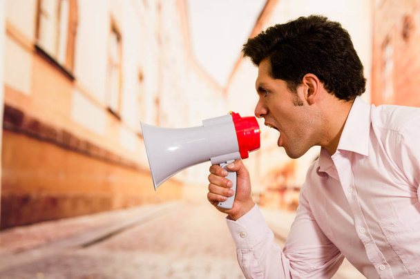 Close up of a handsome man screaming with a megaphone in a blurred background - Foto, Imagen
