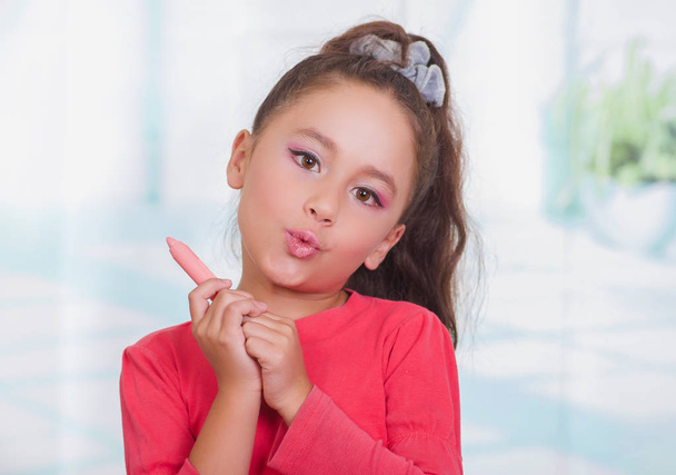 Close up of little beautiful girl holding in her hands a lipstick in a blurred background - Fotografie, Obrázek