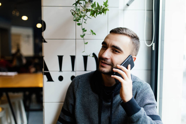 Handsome young man talking on phone and smiling at modern cafe - Photo, image