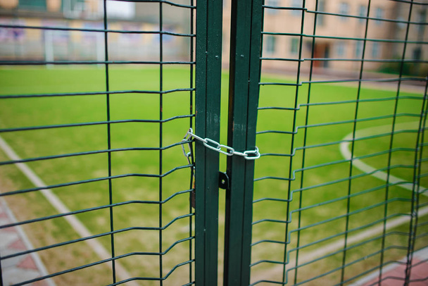 Sulje metallinen verkko-muotoinen vihreä aita, joka on suljettu ja kääritty ketjun taustalla koulun jalkapallokenttä
 - Valokuva, kuva