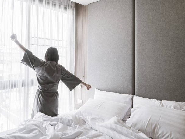 Vrouw die zich uitstrekt in bed na het wakker worden, achteraanzicht - Foto, afbeelding