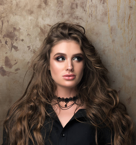 Portrait of beautiful young woman with professional makeup standing against the wall - Photo, Image