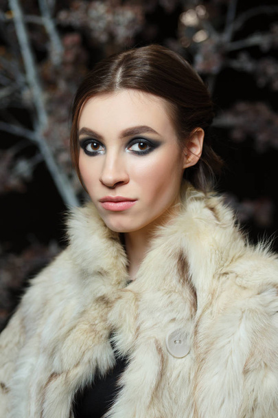 Attractive girl in evening make up and lowered fur coat on dark background - Photo, Image