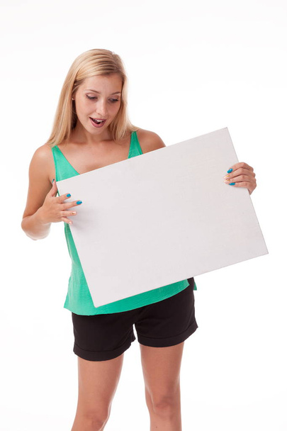 Blonde with long hair posing with white plate. Put a logo, advertisement. Photo on a white background for advertising. shows different postures and emotions. Posing with nameplate on a white background. dressed in a business black suit. skirt  - Zdjęcie, obraz