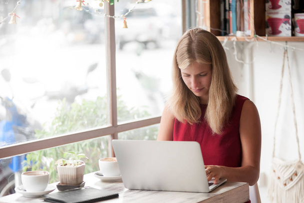 Молодая женщина-фрилансер, печатающая в ноутбуке в кафе
 - Фото, изображение