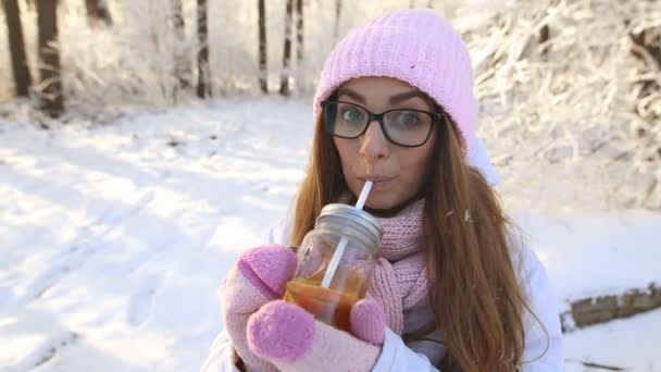 a szép lány a rózsaszín kalapot és ujjatlan, a téli havas erdei teát iszik - Felvétel, videó