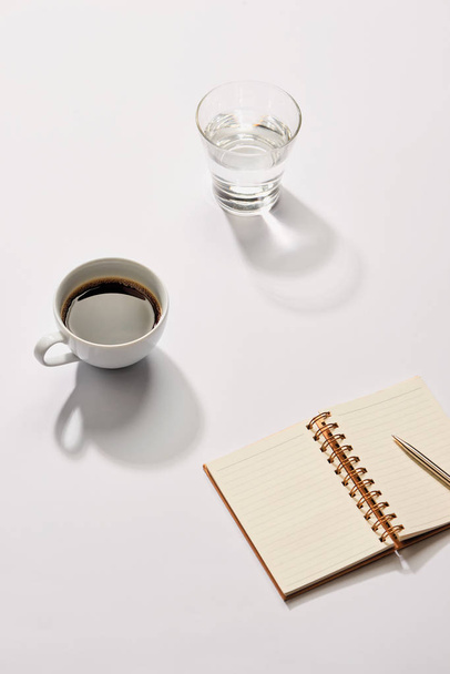 Minimal styled flat lay table with open notebook, pen glass of water and coffee cup. - Fotoğraf, Görsel