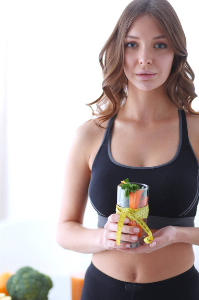 Egy nő kezében egy pohár friss gyümölcssalátával, egy mérőszalaggal az üveg körül.. - Fotó, kép