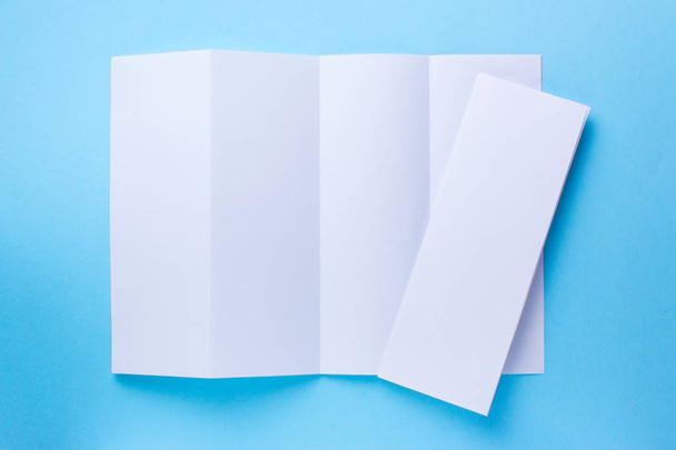 Lehtinen tyhjä Nelinkertainen valkoinen paperi esite mallinnus sinisellä pohjalla. ylhäältä
 - Valokuva, kuva