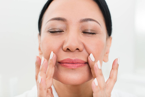 Calm senior woman using cosmetic at spa - Фото, изображение