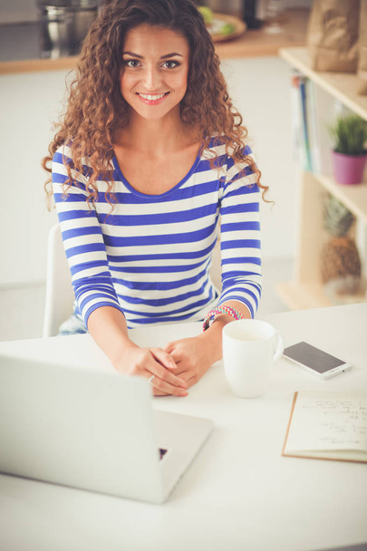 Smiling young woman with coffee cup and laptop in the kitchen at home. Smiling young woman - Foto, afbeelding