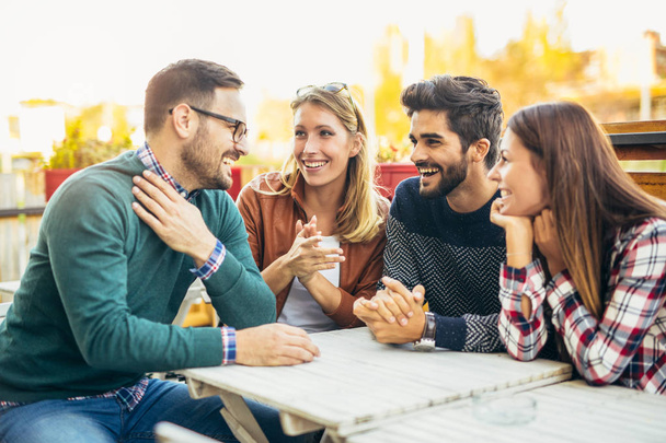 Grupo de cuatro amigos divirtiéndose tomando un café juntos. Dos mujeres y dos hombres en la cafetería hablando riendo y disfrutando de su tiempo - Foto, Imagen