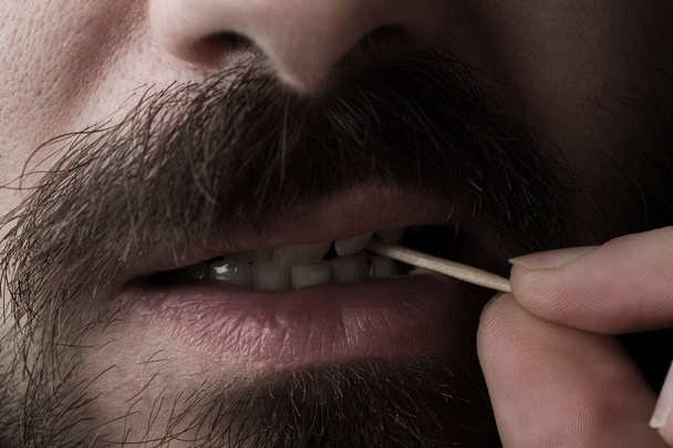 крупним планом бородатий чоловік з дерев'яною зубочисткою
 - Фото, зображення