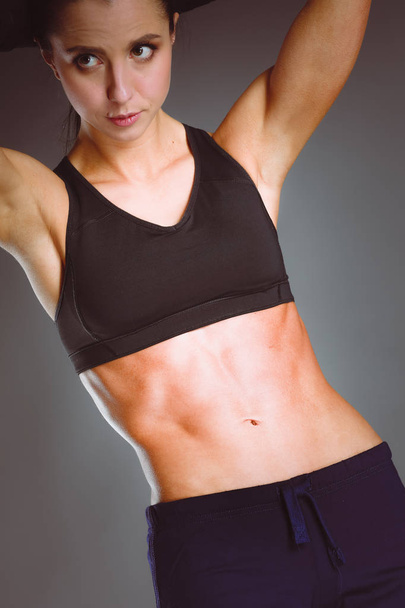 М'язиста молода жінка позує в спортивному одязі на чорному тлі
 - Фото, зображення