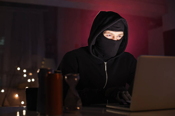暗い部屋でノート パソコンを使用して銃を持つマスクのテロリスト ロイヤリティフリー写真 画像素材