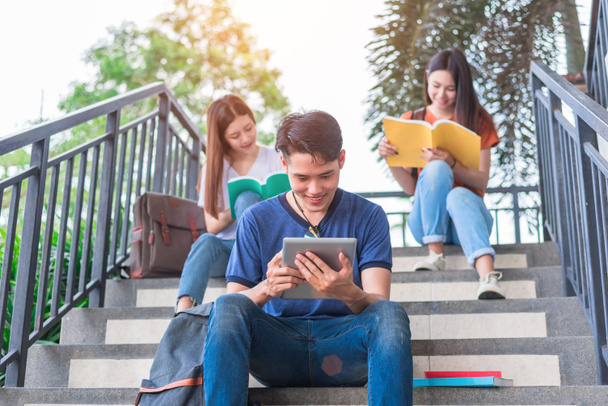 Groupe d'étudiants asiatiques lisant et examinant par manuel et ordinateur portable à l'escalier à l'université. Technologie et éducation concept d'apprentissage. Divertissement et divertissement thème
. - Photo, image