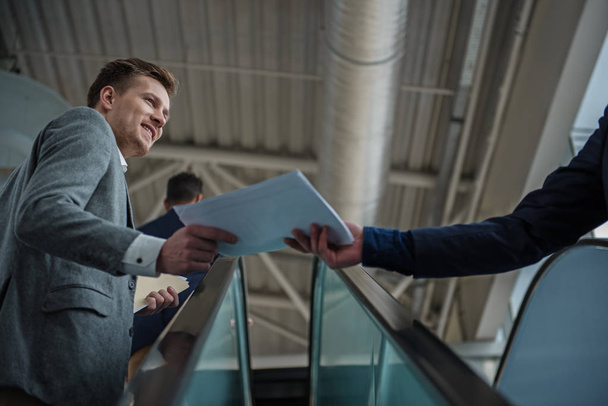 Cheerful guy is holding contract on escalator together with coworker - Foto, Imagem