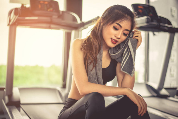 Woman sweats by towel during rest in fitness gym with fitness running equipment. Beauty and relax concept. Gym and fitness training theme   - Photo, Image