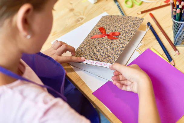 Gros plan angle d'adolescente décorant belle carte-cadeau faite à la main pendant la leçon d'art et d'artisanat à l'école
 - Photo, image