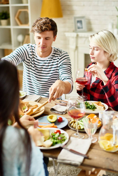 Retrato de grupo de jóvenes amigos cenando juntos, reunidos en una gran mesa con deliciosos platos
 - Foto, imagen