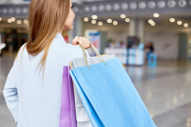Πίσω προβολή πορτρέτο του κομψό νεαρή γυναίκα κρατώντας χάρτινες σακούλες ψώνια στο εμπορικό κέντρο, αντίγραφο χώρου - Φωτογραφία, εικόνα