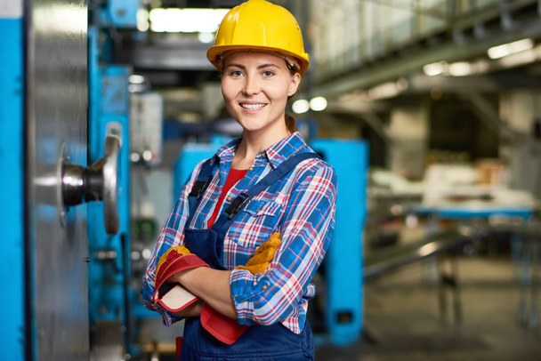 Porträt einer schönen jungen Frau mit Bollenhut, die selbstbewusst in die Kamera lächelt und die Arbeit in einer modernen Fabrik genießt - Foto, Bild