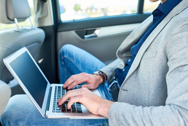 Side view closeup of successful businessman using laptop in back seat of luxury car while working with internet - Foto, Imagen
