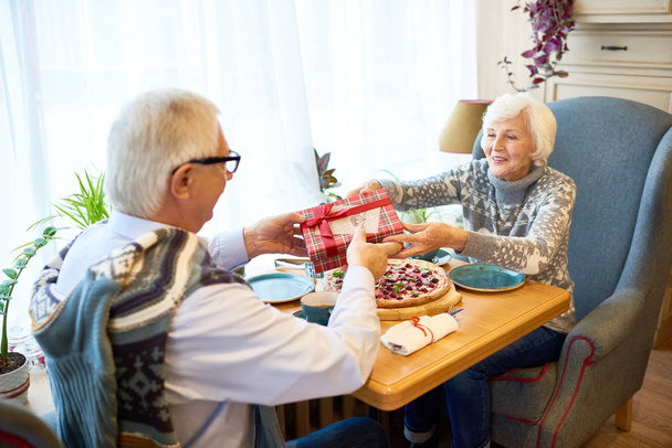 Retrato de feliz pareja de ancianos disfrutando de las vacaciones de Navidad juntos, el intercambio de mesa de regalo en la cafetería
 - Foto, imagen