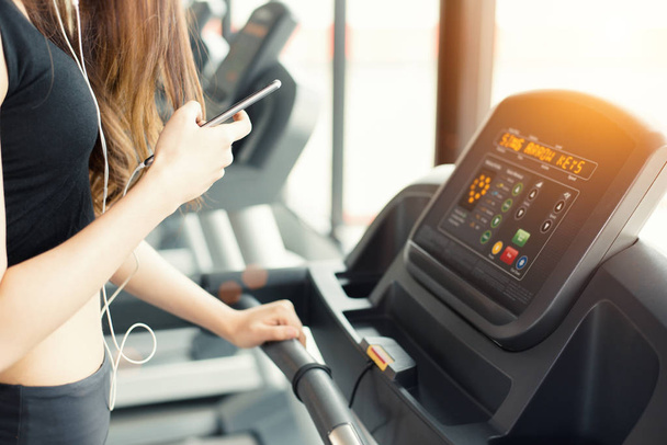 Asian woman using smart phone when workout or strength training at fitness gym on treadmill. Relax and Technology concept. Sports Exercise and Health care theme. Happy and Comfortable mood. - Foto, immagini