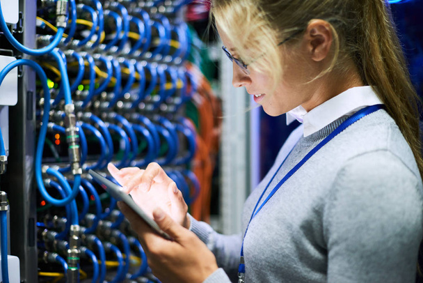 Retrato de vista lateral de mulher jovem usando óculos usando tablet digital em pé contra armários de servidor no data center
 - Foto, Imagem