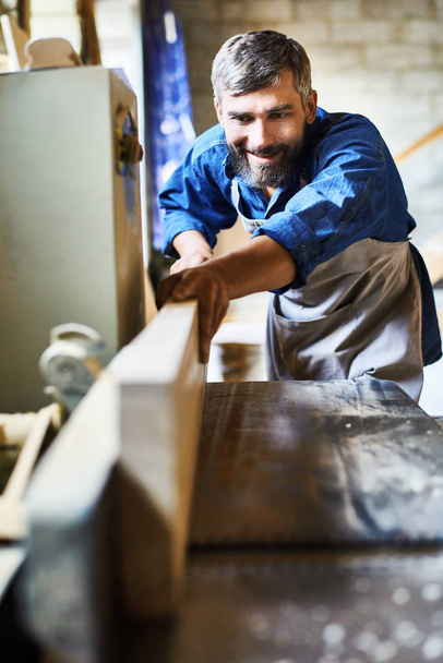 Портрет кваліфікованого бородатого теслі, який щасливо посміхається під час роботи з деревом у столярній майстерні
 - Фото, зображення