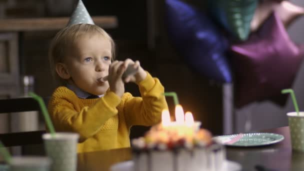 Ładny toddler chłopiec dmuchanie róg urodziny w tabeli - Materiał filmowy, wideo