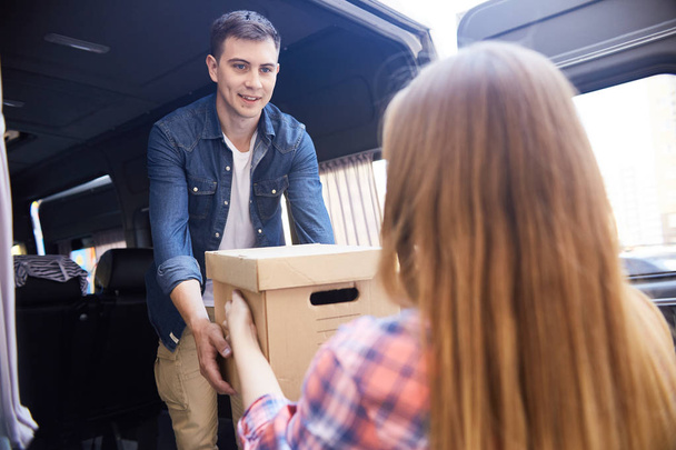 Портрет щасливого молодого чоловіка, який бере картонні коробки від дружини і завантажує їх у рухомий фургон
 - Фото, зображення