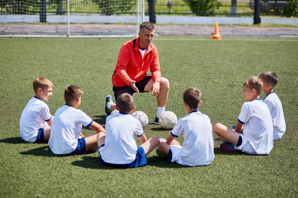 Portrait de l'équipe de garçons assis devant l'entraîneur sur le terrain de football en écoutant la conférence du jeu
 - Photo, image