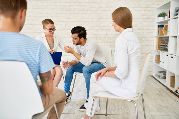 Portrait of young man crying in support group sharing problems with female psychiatrist and other participants in circle - Photo, Image