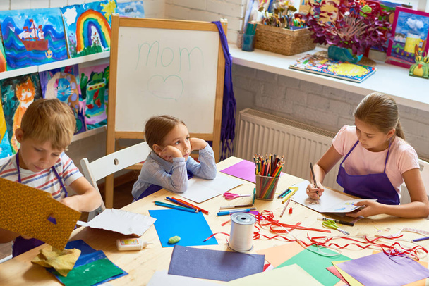 Groupe d'enfants fabriquant des cartes-cadeaux pour la fête des mères pendant les cours d'art et d'artisanat à l'école
 - Photo, image