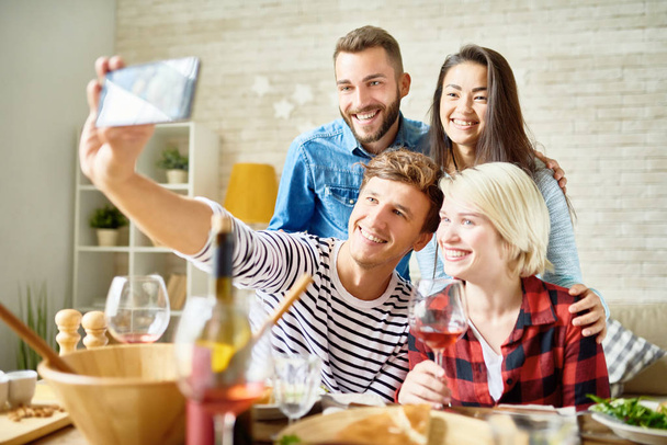 Portrait of four happy friends taking selfie at dinner table while celebrating festive occasion together - Fotoğraf, Görsel