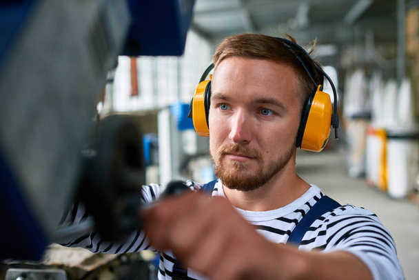 Portrét mladého muže, stisknutím tlačítka na ovládacím panelu při provozu jednotky stroje v dílně - Fotografie, Obrázek
