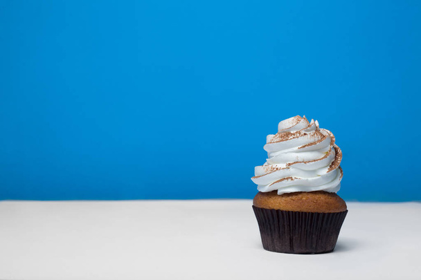cupcake with white cream sprinkled cocoa on a white table on a blue background - Foto, Imagem