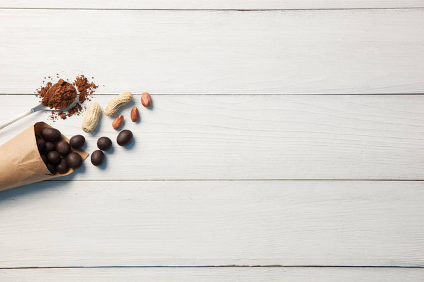 Sweets with peanuts and peanuts with a spoon of cocoa powder on a white wooden background - Foto, Bild