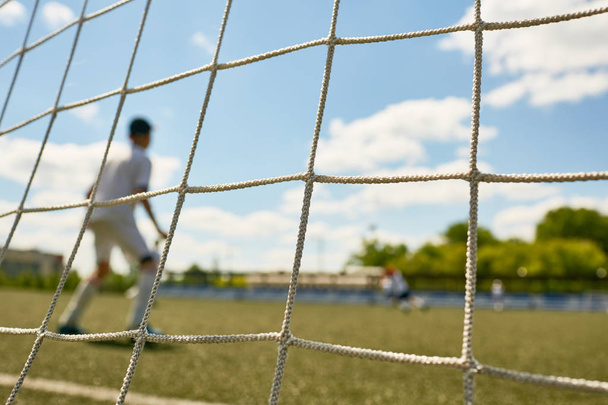 ゲートの網の後ろから撮影、少年サッカーのチーム間のマッチの間にゲートに立っている十代のゴールキーパーの背面縦 - 写真・画像