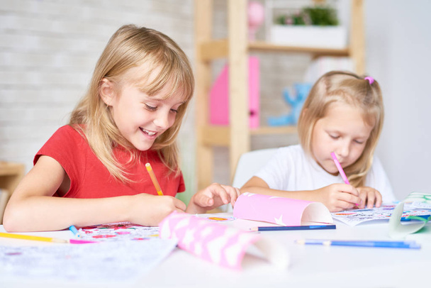 Pretty little participants of drawing class sitting at desk and coloring pictures with felt-tip pens, blurred background - Valokuva, kuva
