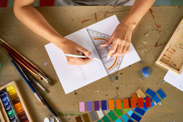 Boven weergave close-up van onherkenbaar jonge vrouw opstellen schetsen met potlood voor kunst en ambacht project zitten op houten tafel in werkplaats - Foto, afbeelding