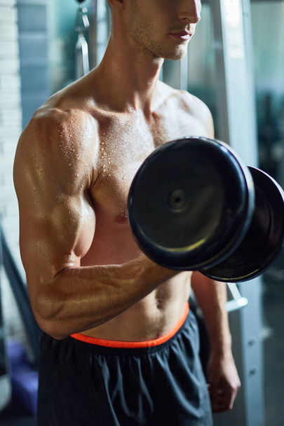 Mid-section portrait of muscular sportsman working out with dumbbell in modern gym - Photo, Image