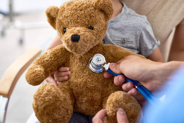 Γκρο πλαν πυροβολισμό αγνώριστος doctor χρησιμοποιώντας στηθοσκόπιο προκειμένου να εξετάσει το teddy αρκούδα που ανήκουν στον μικρό ασθενή - Φωτογραφία, εικόνα