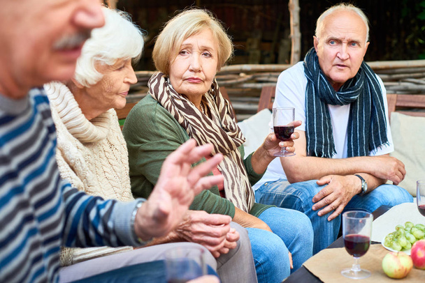 langersehntes Treffen von Kindheitsfreunden: Seniorinnen und Männer in warmen Kleidern sitzen am Café-Tisch im Freien und erinnern sich an angenehme Momente aus ihrer Vergangenheit - Foto, Bild