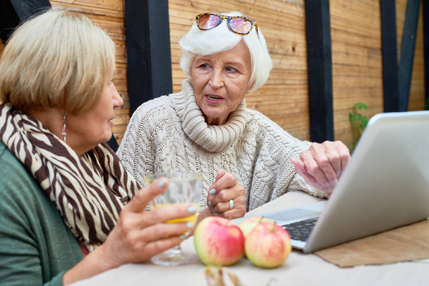 Tech-savvy donne anziane che utilizzano il computer portatile moderno mentre seduto al caffè all'aperto e godendo di succo appena spremuto
 - Foto, immagini